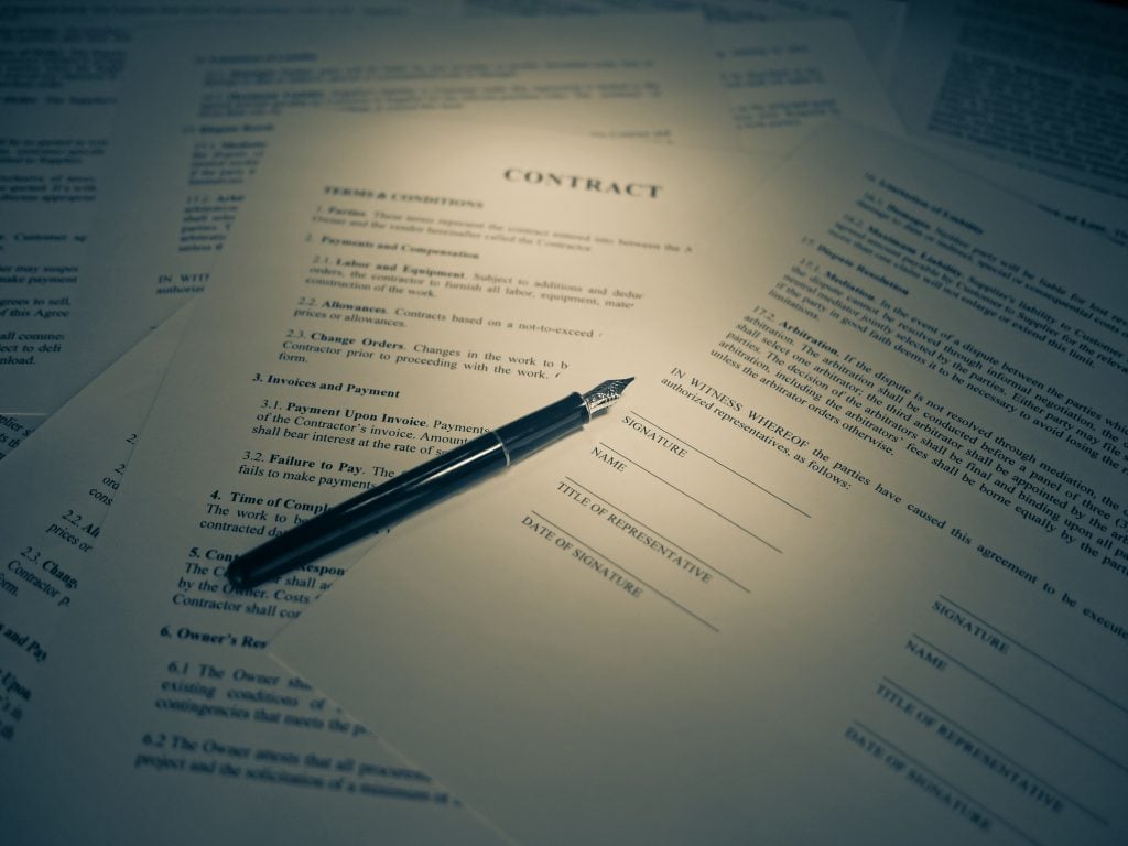 Stack of legal contract documents on a desk awaiting signature, illustrating CRM contract lifecycle management
